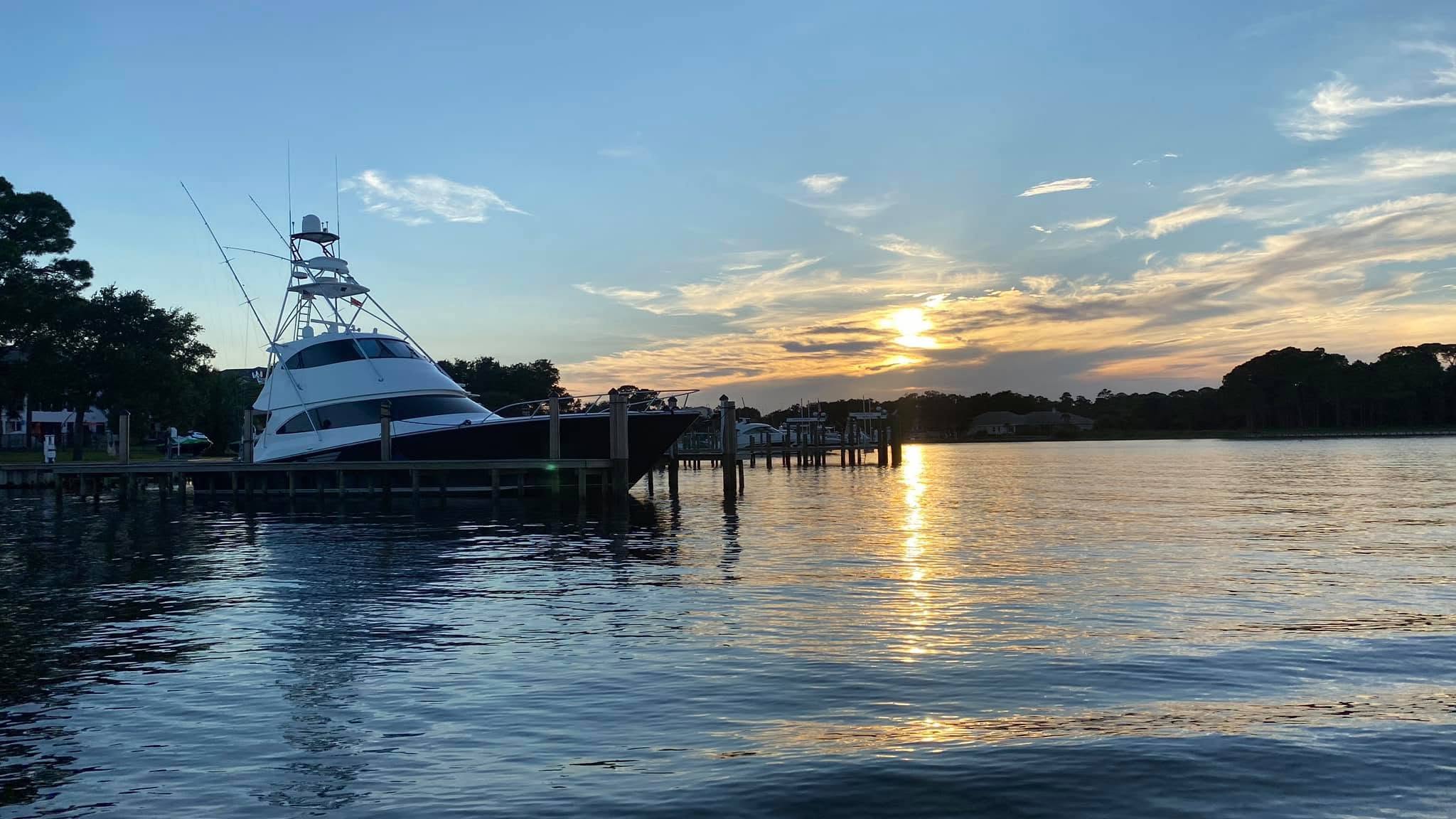 Boat docked at sunset with trees silhouetted against a colorful sky.