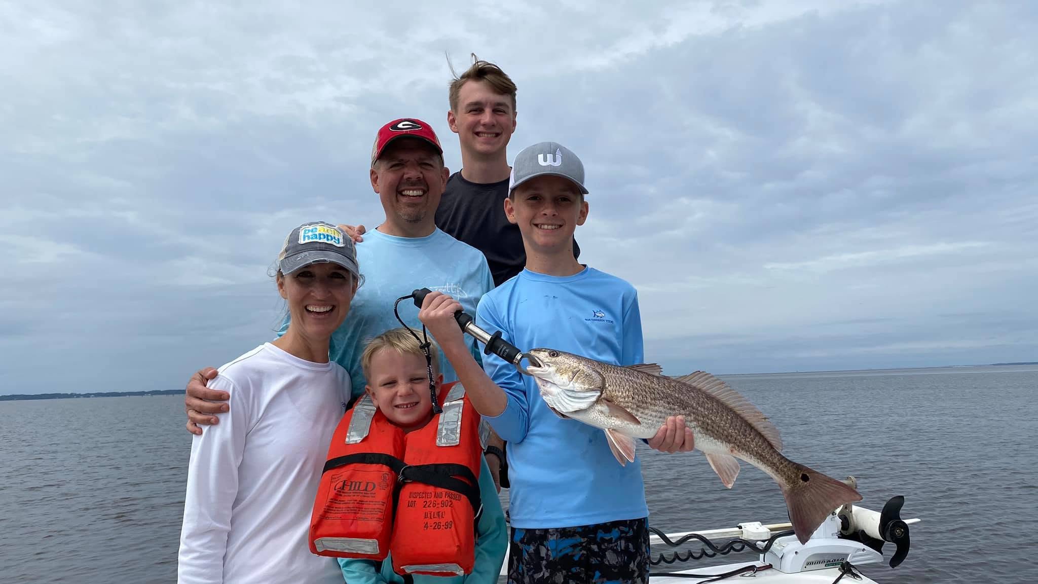 Family smiling on a boat with a child holding a fish, cloudy sky backdrop.