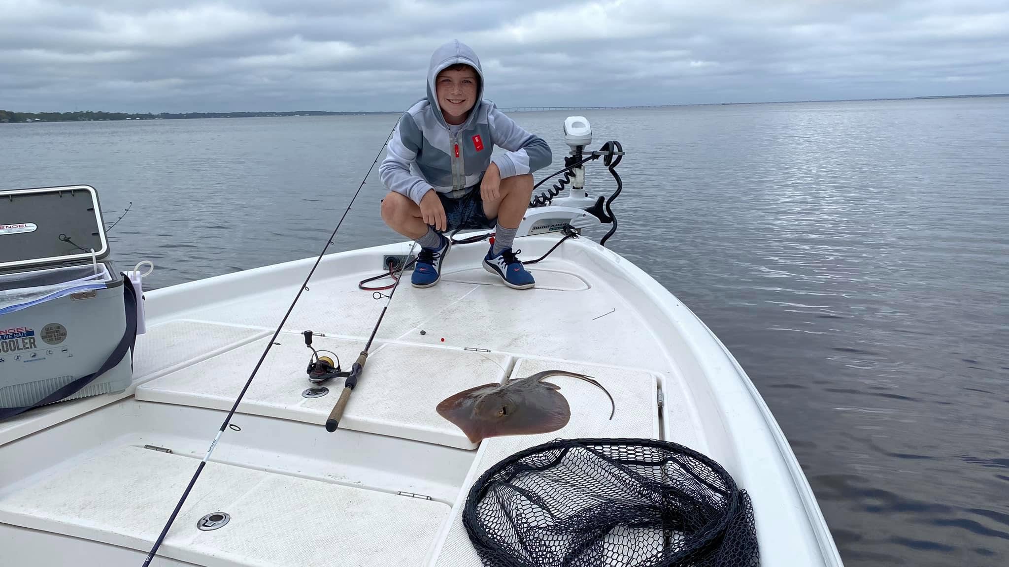 Person in hoodie squatting on boat deck with fishing gear and stingray.