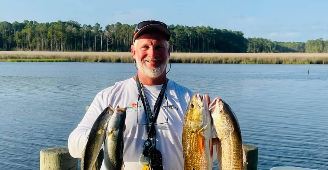 Person on dock holding two fish in each hand by a lake.