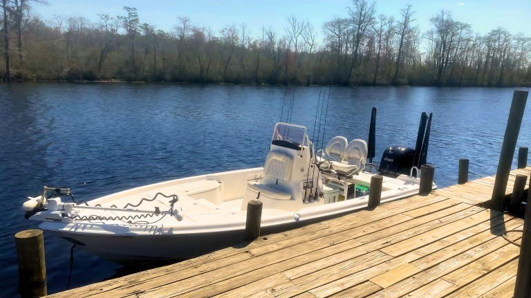 Small fishing boat docked on a calm river with a wooded shoreline.