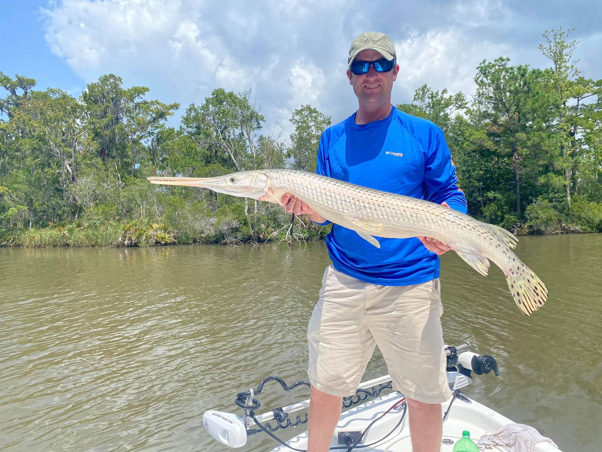 Man in a blue shirt holding a large fish on a boat near a river.