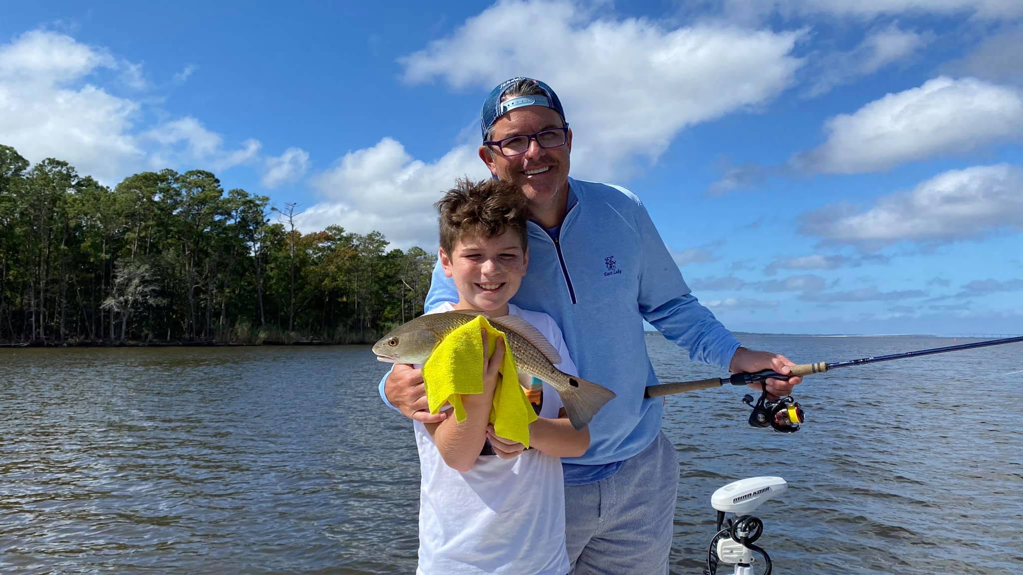 Man and boy holding fish on a boat in a lake.