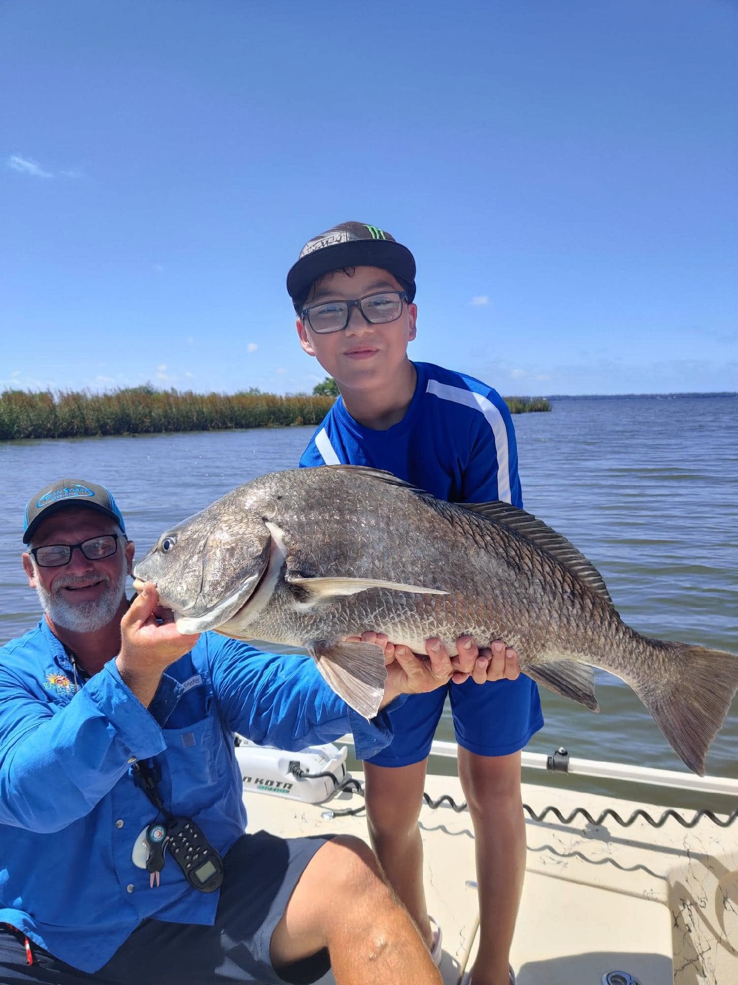 Two people on a boat holding a large fish at the lake.