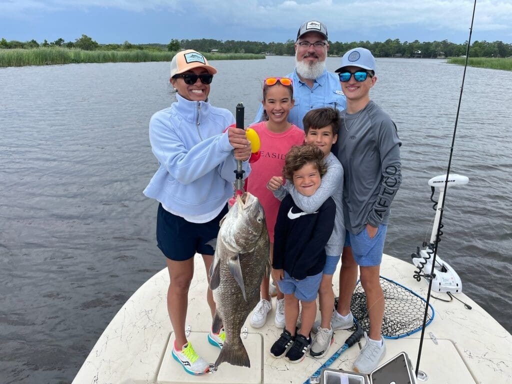 Group of people holding a large fish on a boat by a lake.