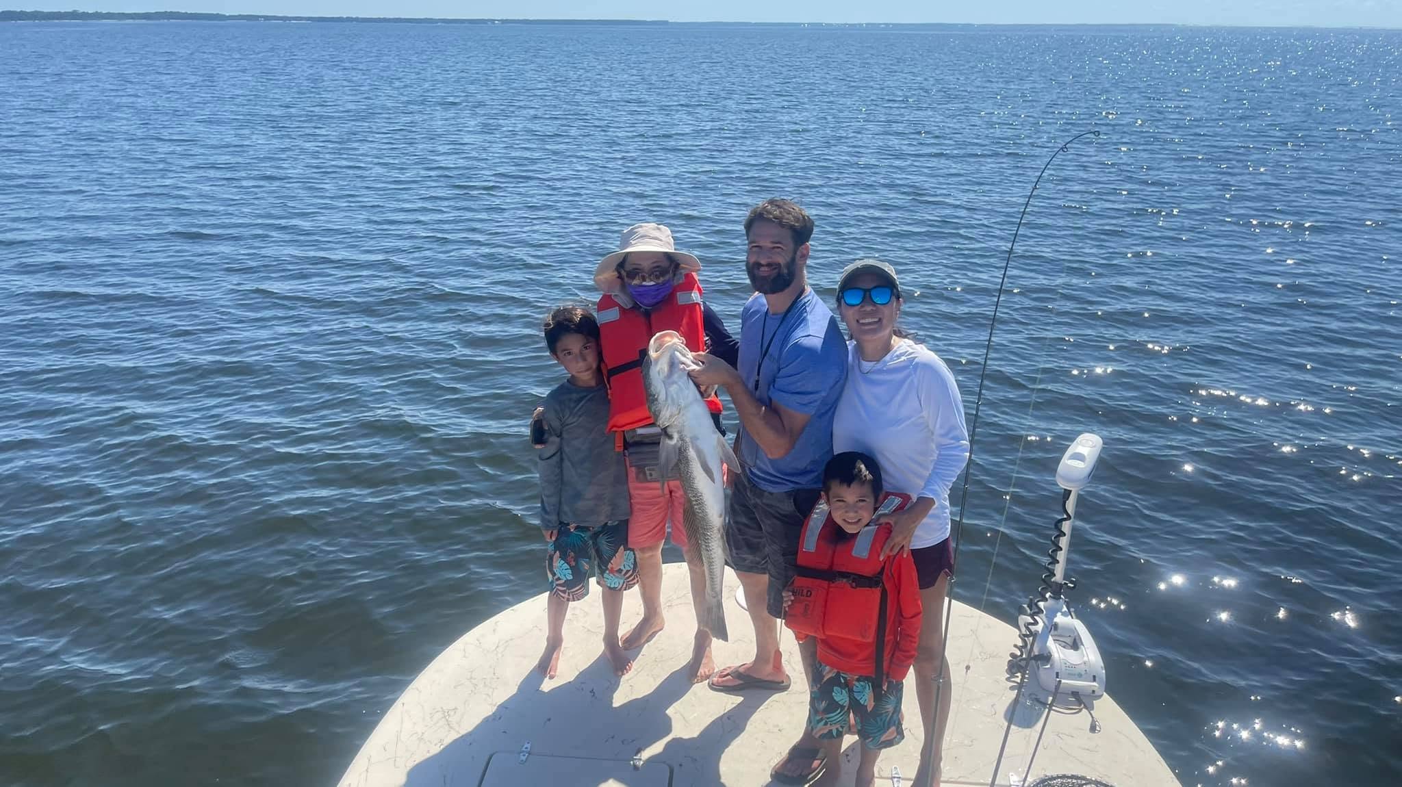 Family on a boat holding a fish with a wide ocean view.