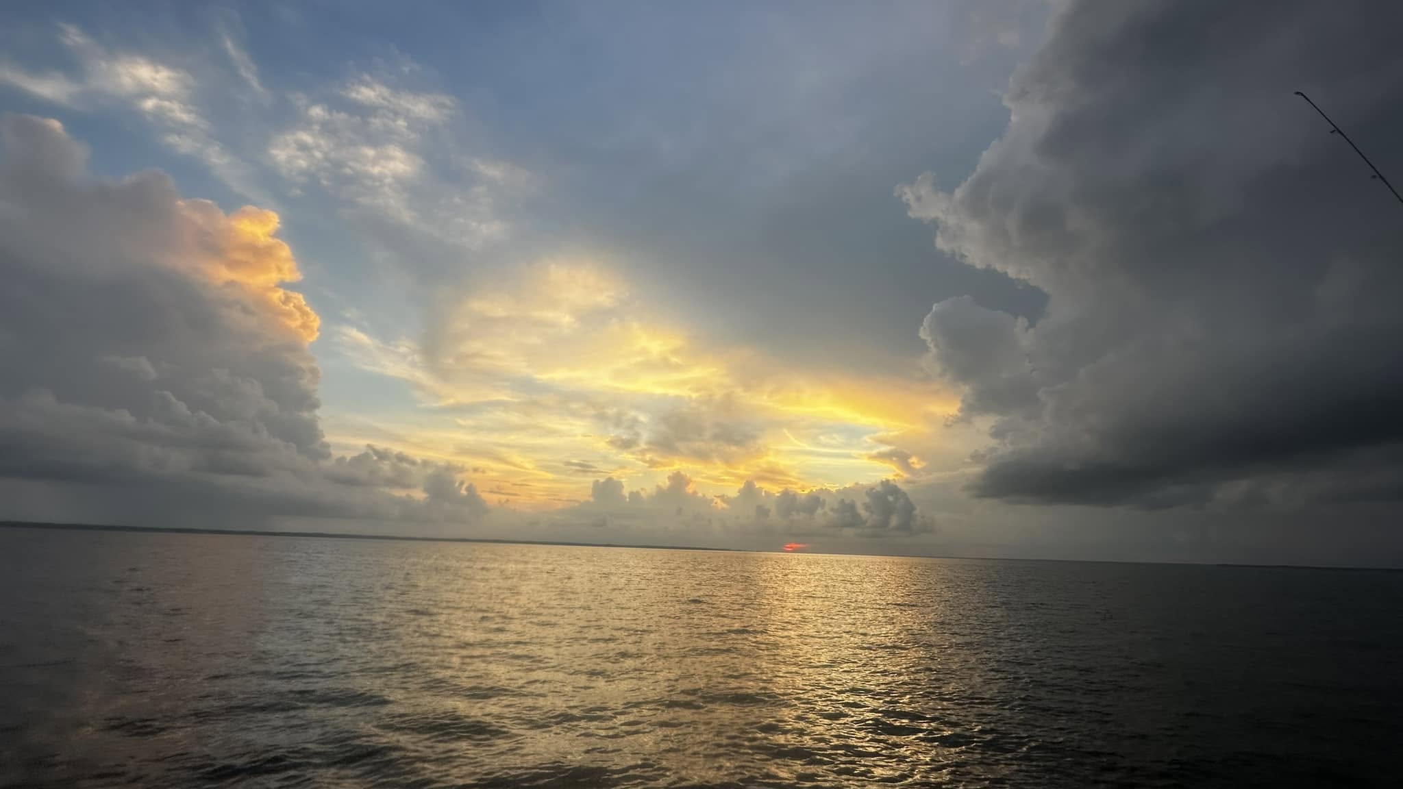 Sunset over calm sea, clouds partly covering the sky.