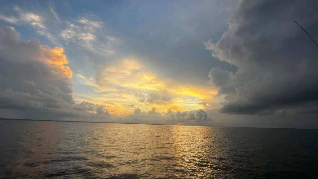 Sunset over calm sea, clouds partly covering the sky.