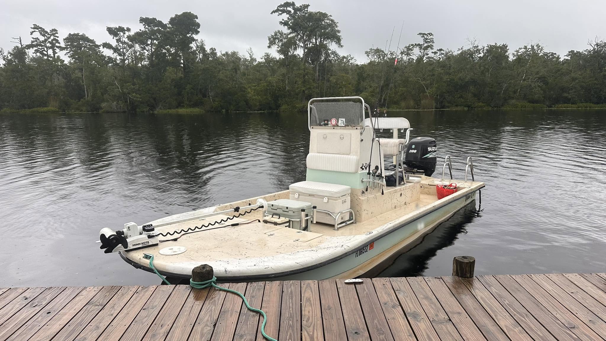 Docked small fishing boat on a calm river near trees.