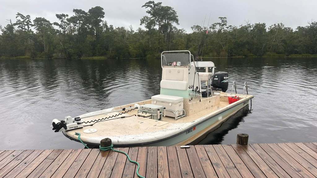 Docked small fishing boat on a calm river near trees.