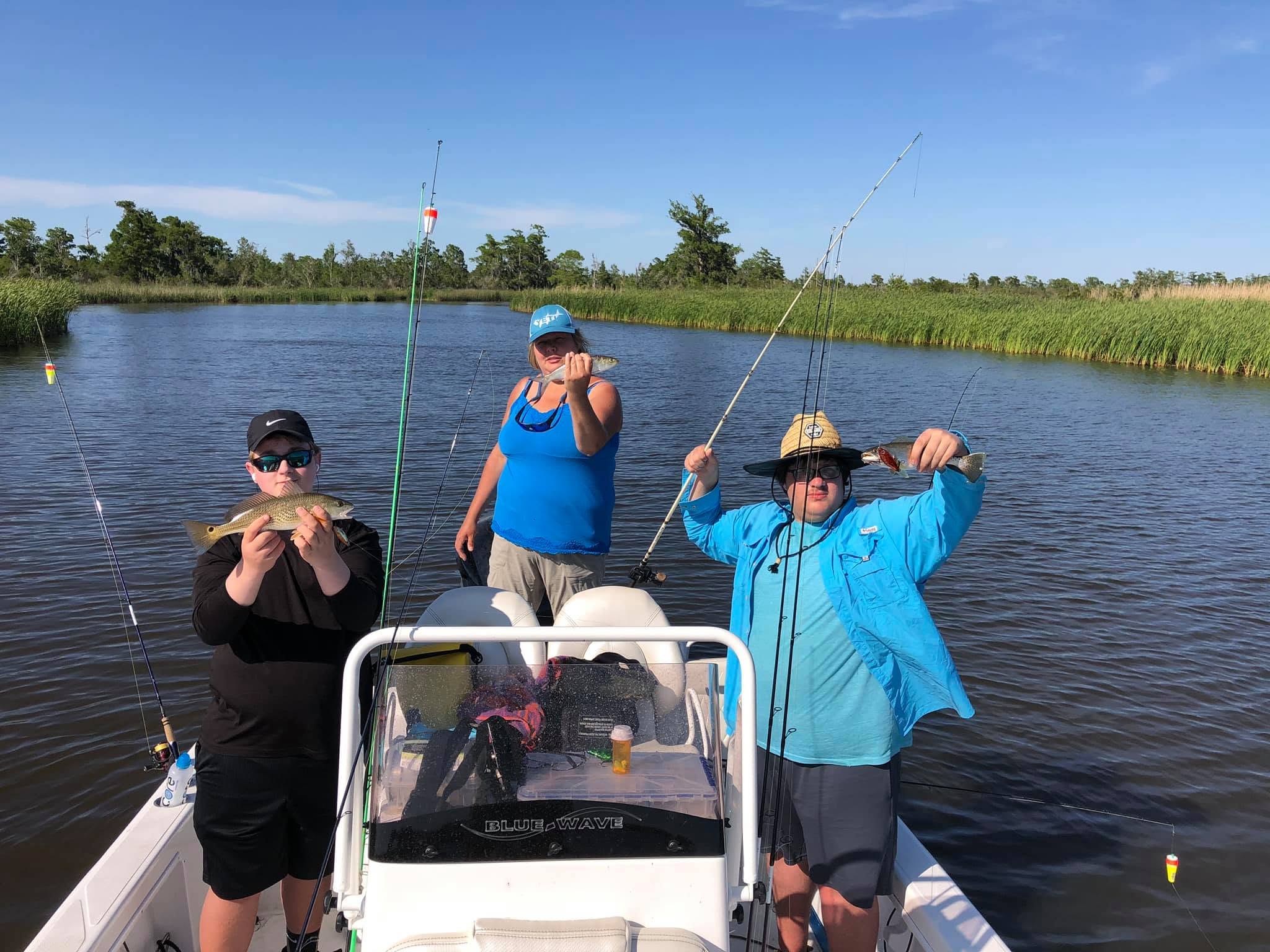 Three people on a boat holding fishing rods and caught fish in a lake.